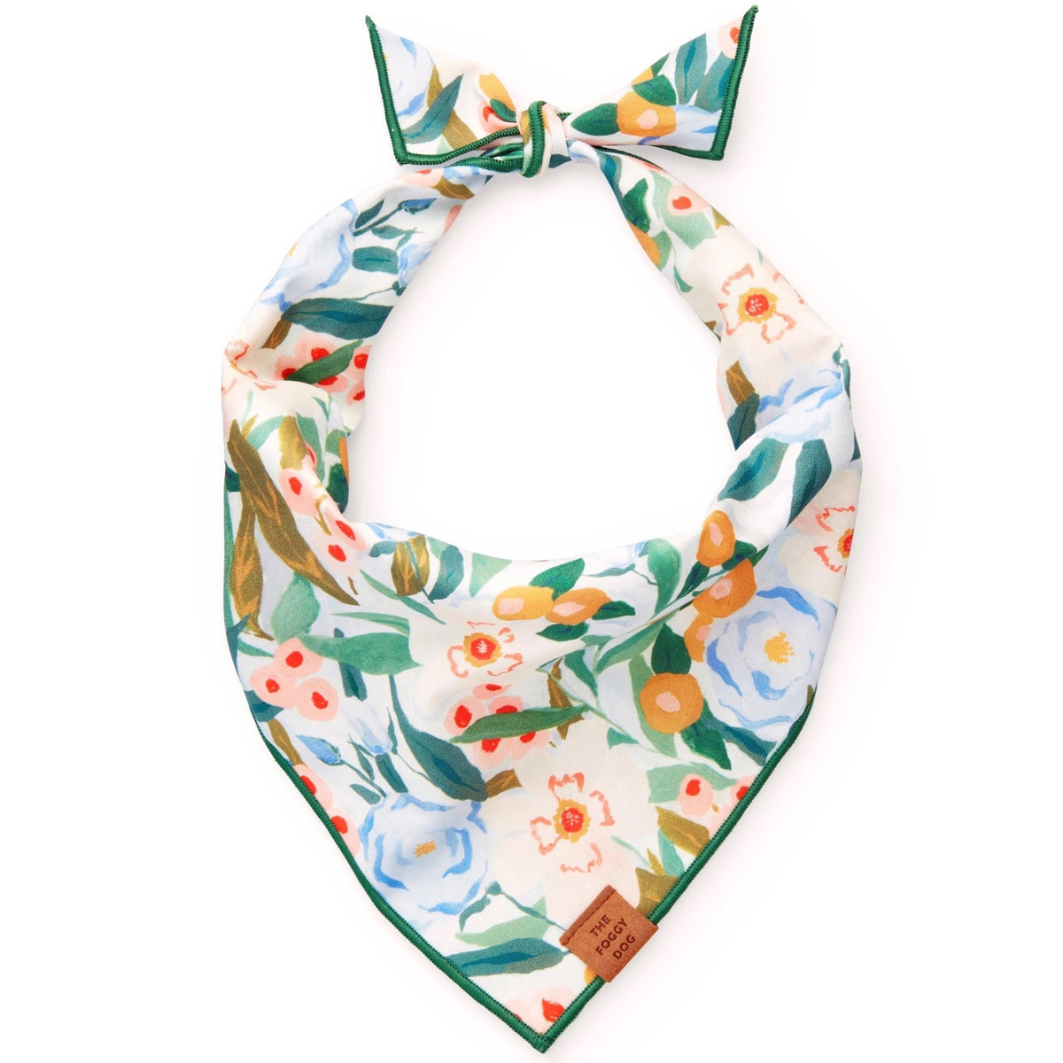 The BANDANA by THE FOGGY DOG is a handmade triangular floral accessory showcasing a vibrant array of colorful flowers in shades of blue, yellow, orange, and green. Its edges are elegantly trimmed in green, and it features a stylish knot at the top. A small leather tag at the point reads &quot;The Foggy Dog.&quot; This beautiful piece is made in San Francisco.