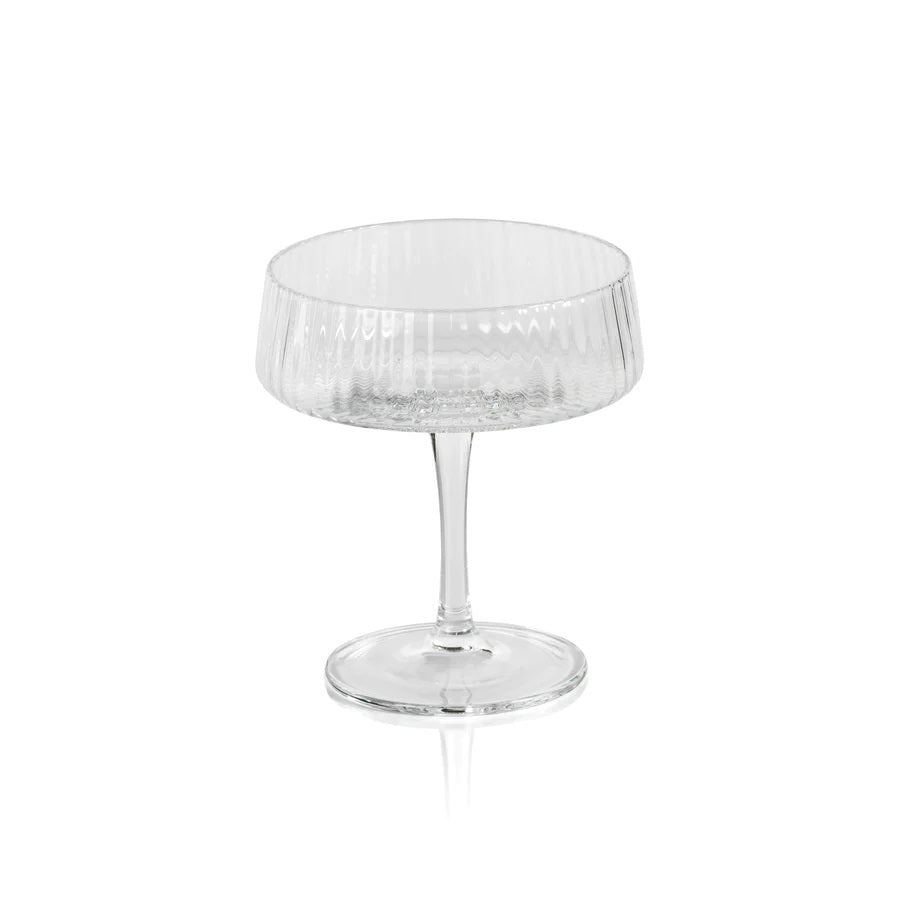 The FLUTED TEXTURED MARTINI GLASS by ZODAX stands empty against a white background, showcasing its wide, shallow bowl perched on a thin stem. Vertical ridges adorn the clear surface of the glass, adding texture to its elegant design. A flat, round base ensures stability.