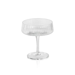 The FLUTED TEXTURED MARTINI GLASS by ZODAX stands empty against a white background, showcasing its wide, shallow bowl perched on a thin stem. Vertical ridges adorn the clear surface of the glass, adding texture to its elegant design. A flat, round base ensures stability.