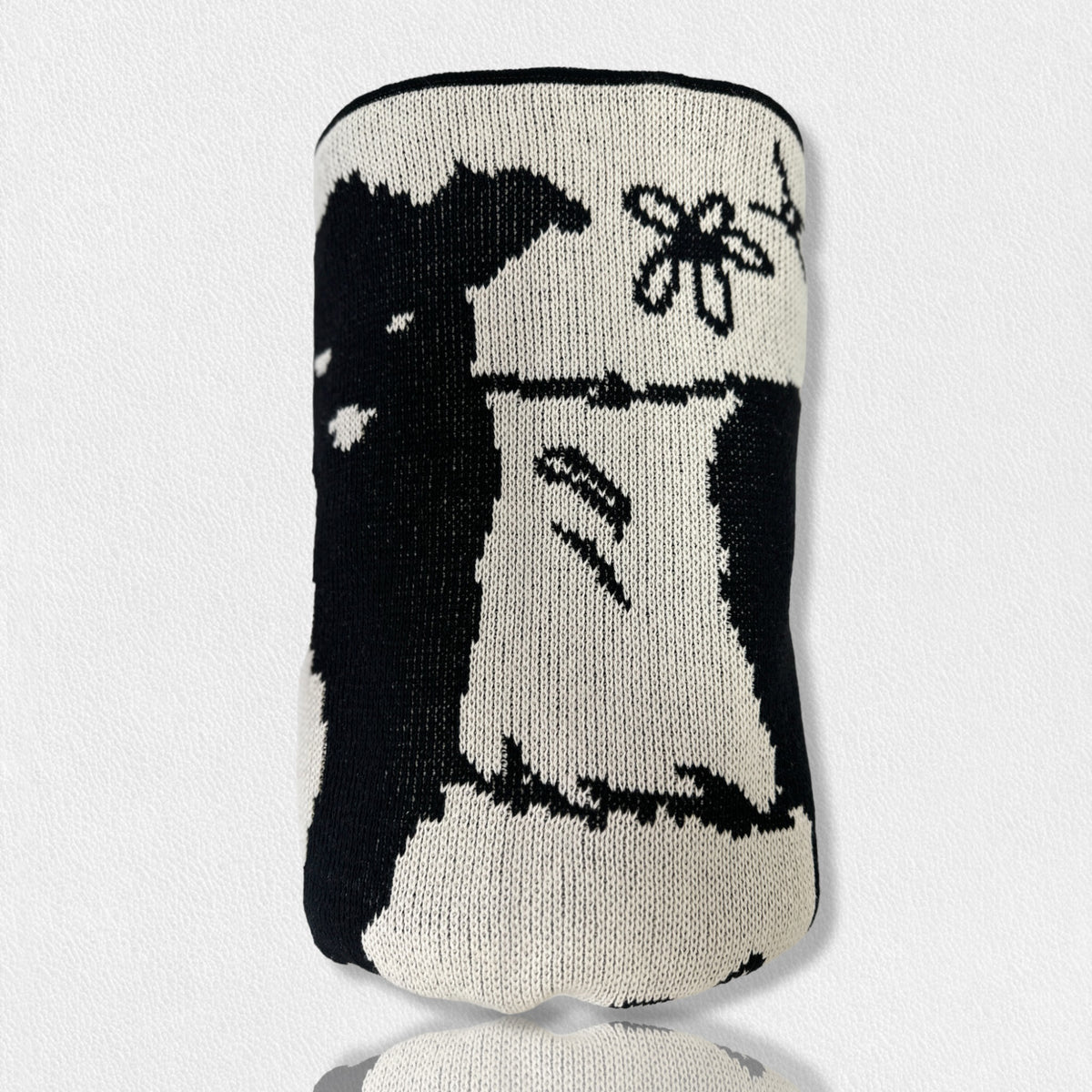 Presenting the FEARRINGTON SIGNATURE COLLECTION - BELTIE BARNYARD KNIT THROW by CALHOUN &amp; CO., this cylindrical knitted item showcases a black and white design with a close-up of a rabbit holding a flower. Made in America, it features minimal detailing that emphasizes contrasting shades, creating a simple and stylized depiction of the rabbit and flower.