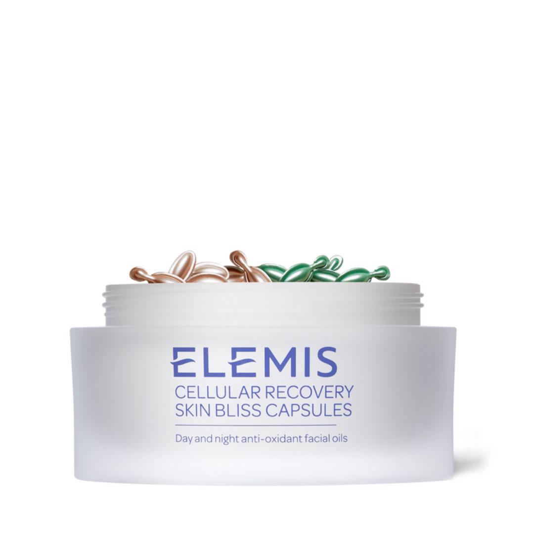 A white container with a translucent matte finish is open to reveal mixed pink and green capsule-shaped facial oils. The label reads &quot;ELEMIS - CELLULAR RECOVERY SKIN BLISS CAPSULES by ELEMIS - STEINER, Day and night antioxidant facial oils for anti-ageing.