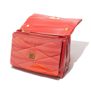 Presenting the VINTAGE SCARF AND LEATHER HANDBAG by MILANO MM33, a vibrant rectangular accessory adorned with a bright orange and pink striped pattern. This handbag, evocative of classic scarf styles, boasts elegant gold chains for shoulder straps and a prominent shiny gold buckle on the front flap. Made from soft fabric and luxurious leather, it is showcased against a pristine white background.