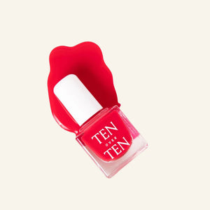 A glass bottle of TENOVERTEN - NAIL POLISH from the brand TEN OVER TEN, featuring a white cap and a dusty pink nail color. The front label displays "TEN OVER TEN" in white uppercase letters. This vegan, eight-free formula ensures both beauty and peace of mind. The background is plain and light-colored.