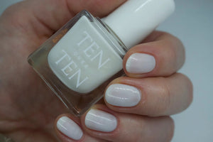 A glass bottle of TENOVERTEN - NAIL POLISH from the brand TEN OVER TEN, featuring a white cap and a dusty pink nail color. The front label displays "TEN OVER TEN" in white uppercase letters. This vegan, eight-free formula ensures both beauty and peace of mind. The background is plain and light-colored.