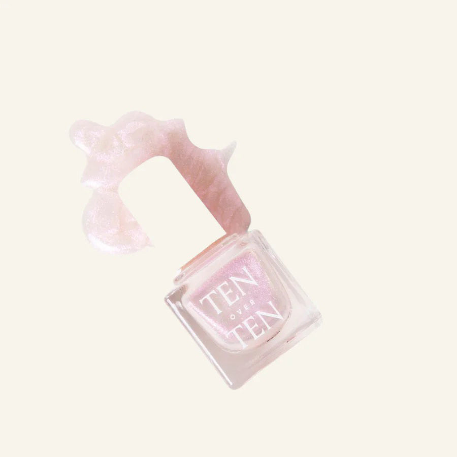 A glass bottle of TENOVERTEN - NAIL POLISH from the brand TEN OVER TEN, featuring a white cap and a dusty pink nail color. The front label displays "TEN OVER TEN" in white uppercase letters. This vegan, eight-free formula ensures both beauty and peace of mind. The background is plain and light-colored.