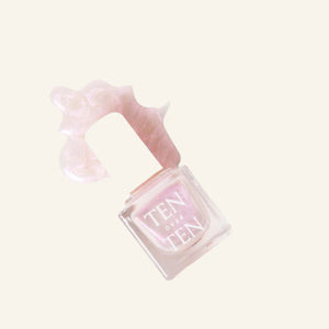 A glass bottle of TENOVERTEN - NAIL POLISH from the brand TEN OVER TEN, featuring a white cap and a dusty pink nail color. The front label displays "TEN OVER TEN" in white uppercase letters. This vegan, eight-free formula ensures both beauty and peace of mind. The background is plain and light-colored.