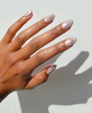 A glass bottle of TENOVERTEN - NAIL POLISH from the brand TEN OVER TEN, featuring a white cap and a dusty pink nail color. The front label displays "TEN OVER TEN" in white uppercase letters. This vegan, eight-free formula ensures both beauty and peace of mind. The background is plain and light-colored.