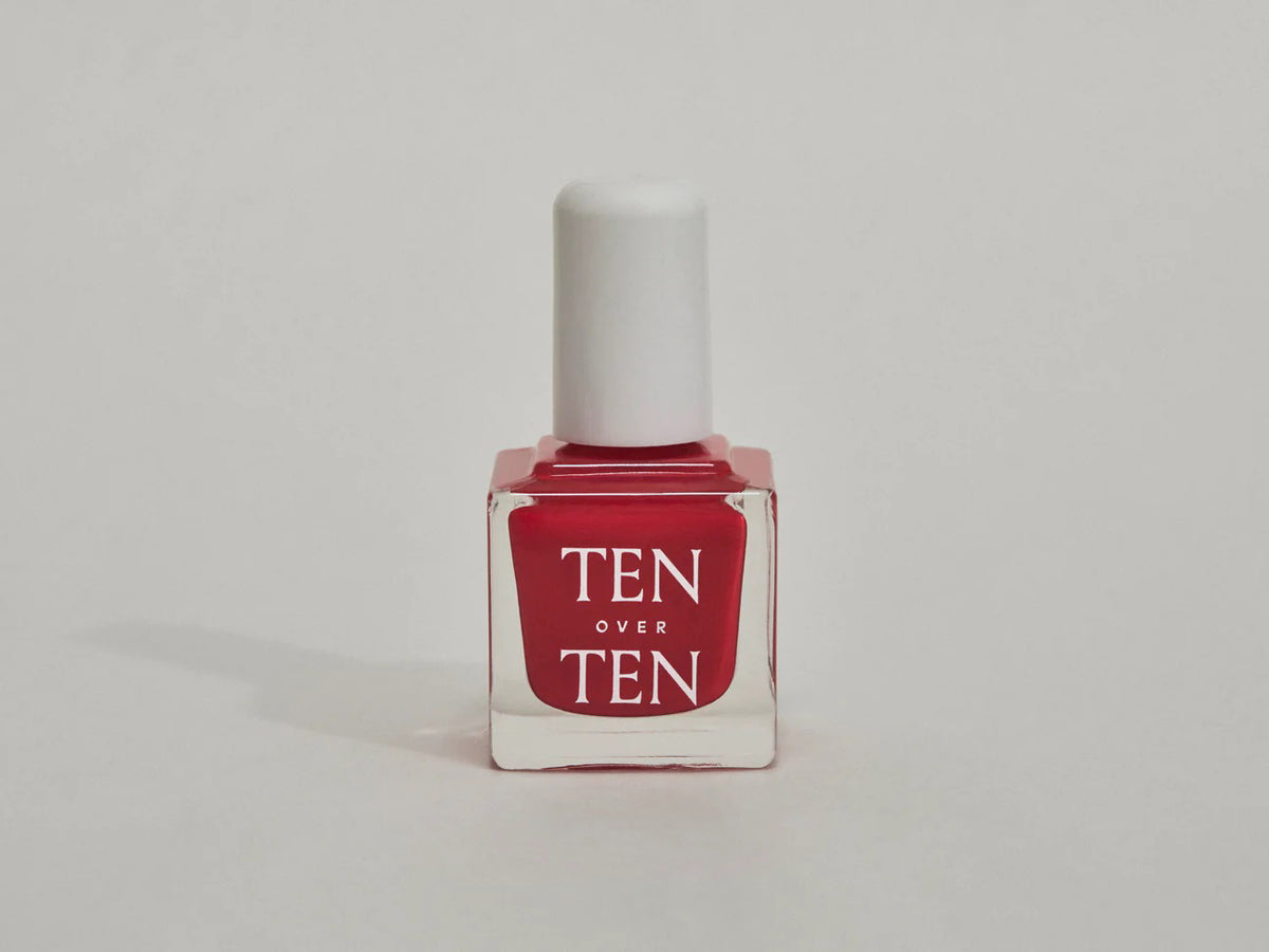 A glass bottle of TENOVERTEN - NAIL POLISH from the brand TEN OVER TEN, featuring a white cap and a dusty pink nail color. The front label displays "TEN OVER TEN" in white uppercase letters. This vegan, eight-free formula ensures both beauty and peace of mind. The background is plain and light-colored.