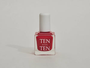 A glass bottle of TENOVERTEN - NAIL POLISH from the brand TEN OVER TEN, featuring a white cap and a dusty pink nail color. The front label displays "TEN OVER TEN" in white uppercase letters. This vegan, eight-free formula ensures both beauty and peace of mind. The background is plain and light-colored.