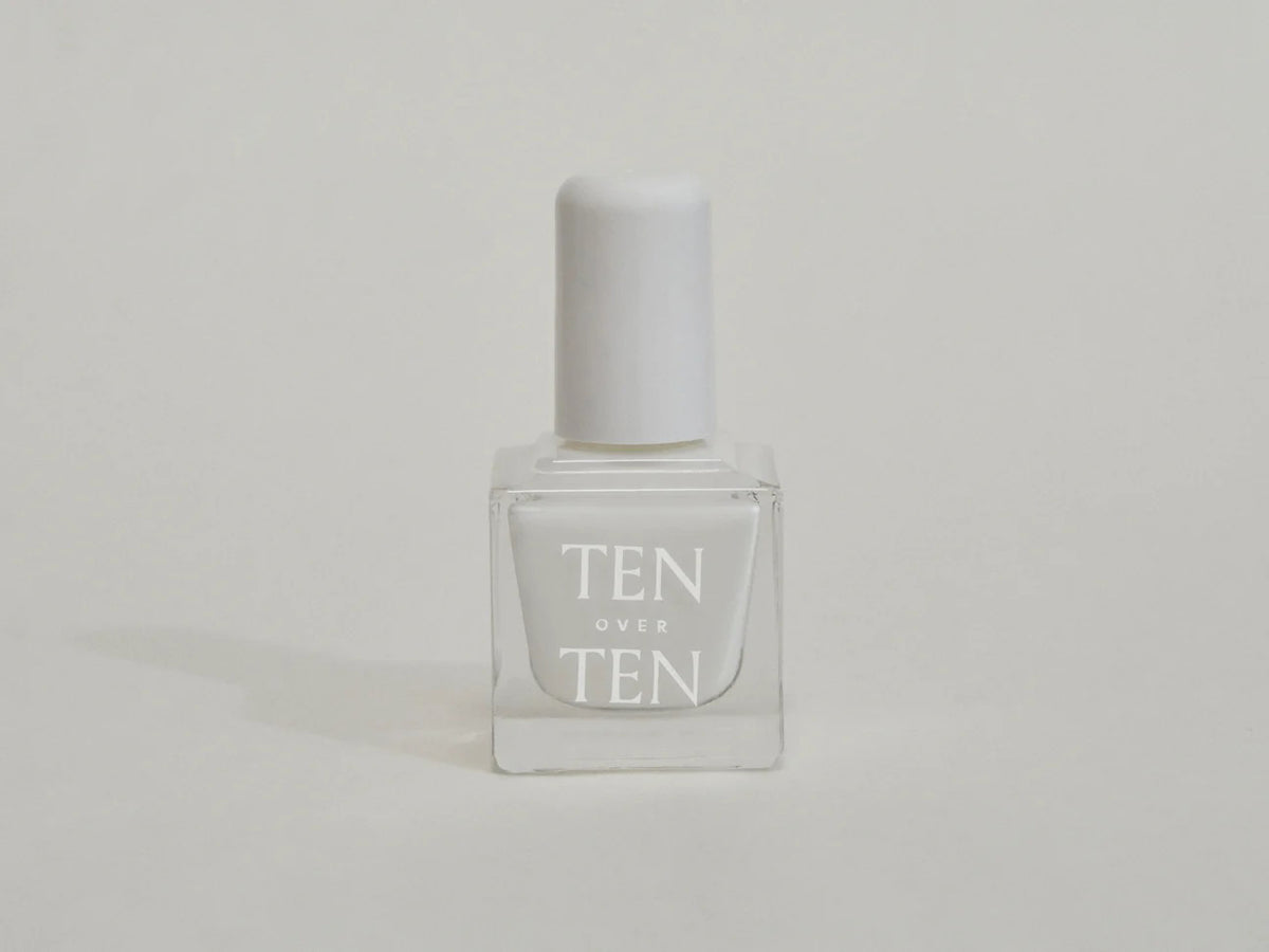 A glass bottle of TENOVERTEN - NAIL POLISH from the brand TEN OVER TEN, featuring a white cap and a dusty pink nail color. The front label displays "TEN OVER TEN" in white uppercase letters. This vegan, eight-free formula ensures both beauty and peace of mind. The background is plain and light-colored.
