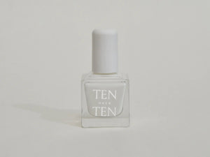 A glass bottle of TENOVERTEN - NAIL POLISH from the brand TEN OVER TEN, featuring a white cap and a dusty pink nail color. The front label displays "TEN OVER TEN" in white uppercase letters. This vegan, eight-free formula ensures both beauty and peace of mind. The background is plain and light-colored.