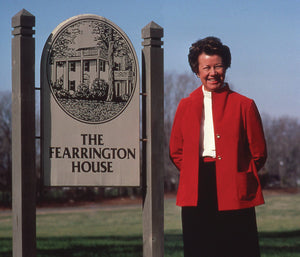 The cover of "Fearrington Signature Collection - The Fearrington House Cookbook by Jenny Fitch" from Belted Goat features an illustrated outdoor garden scene in yellow, with a table set with wine glasses, bread, a pumpkin, and flowers. The subtitle reads "A Celebration of Food Flowers and Herbs.