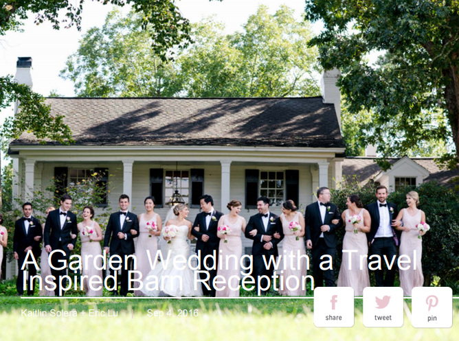 A wedding party poses outdoors in front of a house with a slanted roof and surrounded by trees. The group consists of bridesmaids in light pink dresses and groomsmen in black suits. The text overlay reads, "A Garden Wedding with a Travel Inspired Barn Reception. Fearrington Village