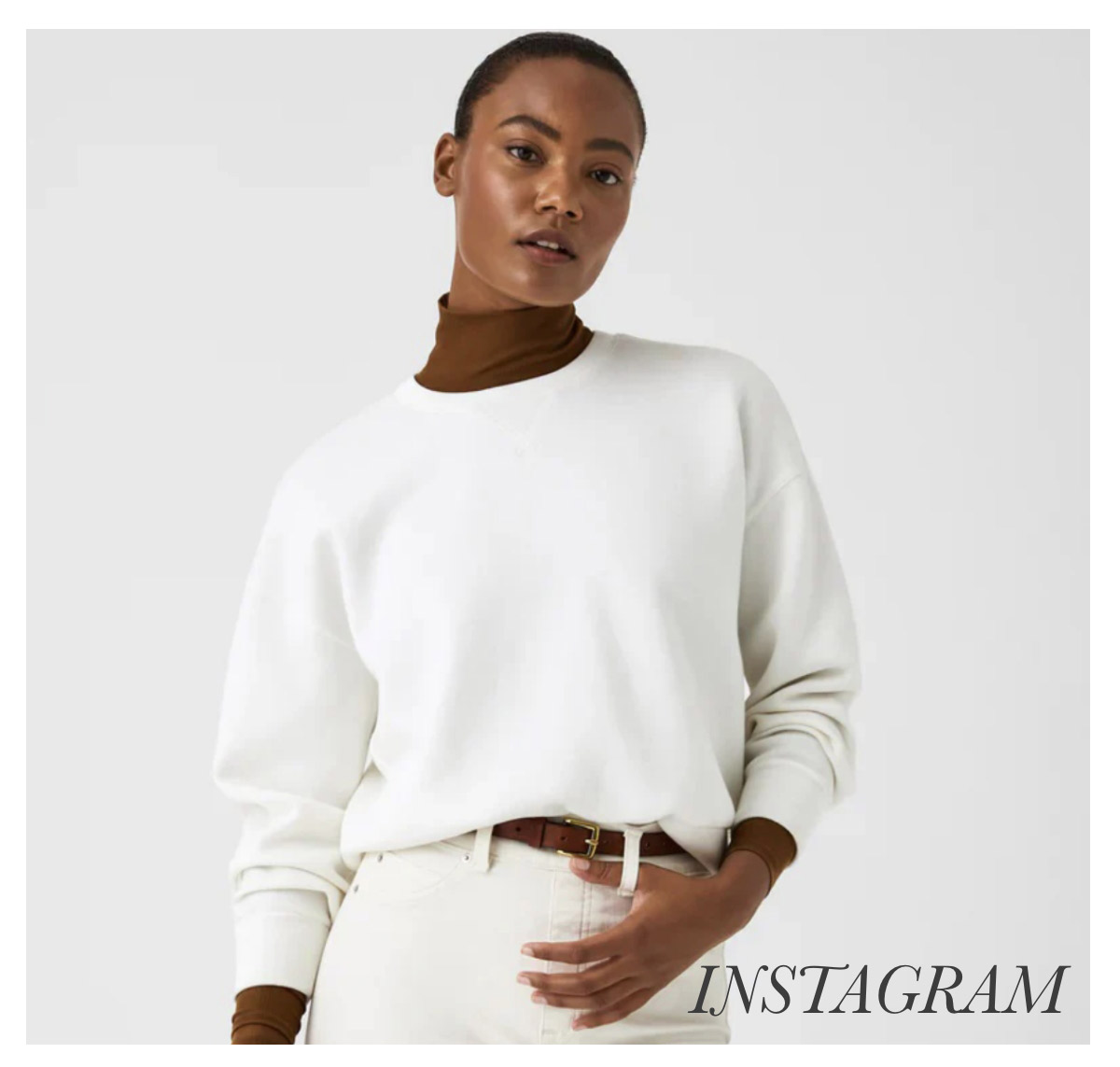 A person with short hair is wearing a white sweatshirt over a brown turtleneck. They are also dressed in white pants with a brown belt. The background is plain white, and the word “INSTAGRAM” is written in the bottom right corner. Fearrington Village