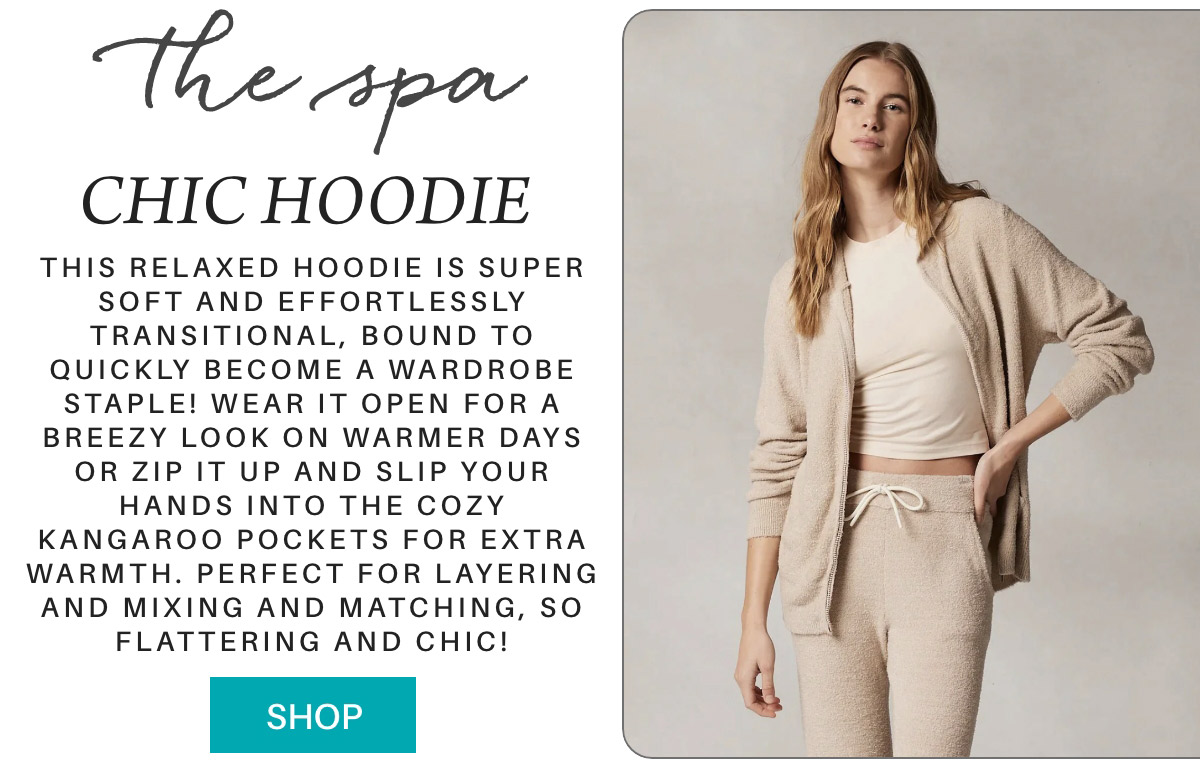 A woman is wearing a beige cozy-looking hoodie and matching pants. The text on the image advertises the "Chic Hoodie," describing it as a relaxed, soft, and transitional wardrobe staple suitable for layering. She stands slightly facing to the side with one hand in her pocket. Fearrington Village