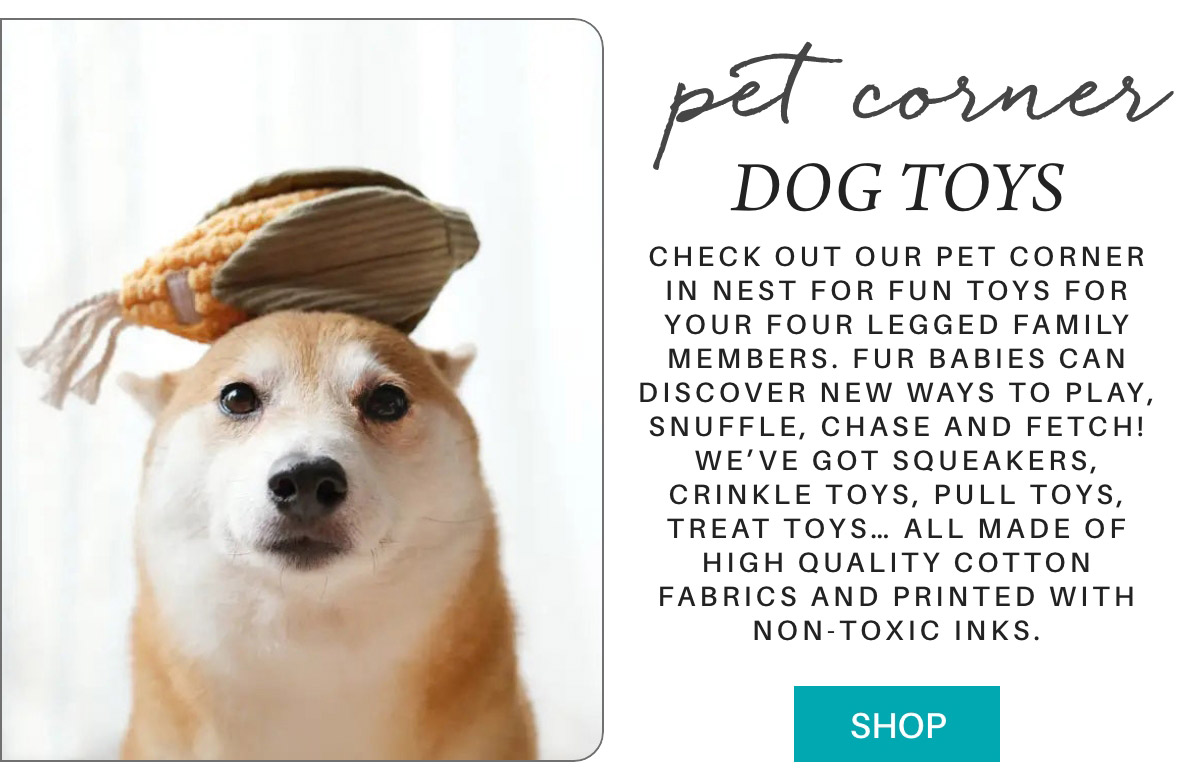 A dog wearing a corn toy looks upward. Text on the image advertises "Pet Corner Dog Toys" with a description of various playful dog toys available, made from high-quality cotton and non-toxic inks. A "Shop" button is visible. Fearrington Village