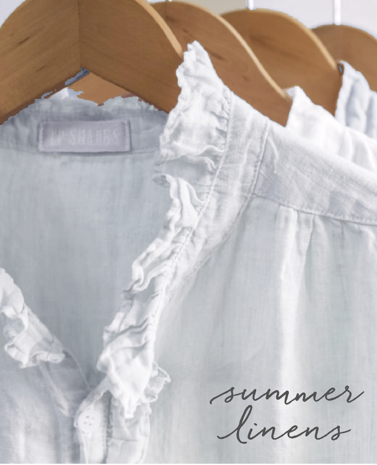 Close-up of white linen shirts hanging on wooden hangers. The shirts feature delicate ruffled collars and are labeled with a faint text on the tag. The phrase "summer linens" is written in elegant cursive at the bottom right. Fearrington Village