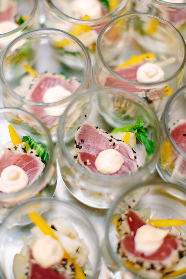 An overhead view of several glass jars filled with a gourmet appetizer. Each jar contains seared tuna slices topped with a dollop of white sauce, and garnished with black sesame seeds, yellow pepper strips, and greens on a bed of finely shredded vegetables. Fearrington Village