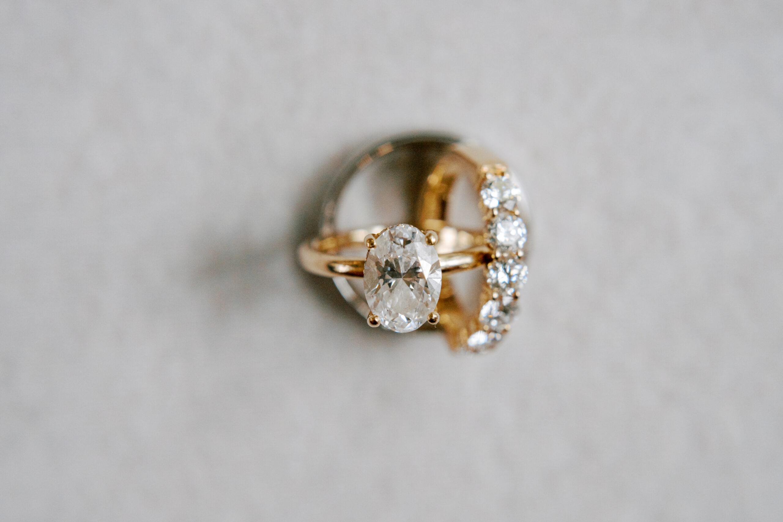 A close-up image of two elegant rings. One ring features a prominent oval-shaped diamond in a prong setting, while the other ring is a band adorned with multiple smaller round diamonds. Both rings are made of gold and are arranged against a plain light background. Fearrington Village