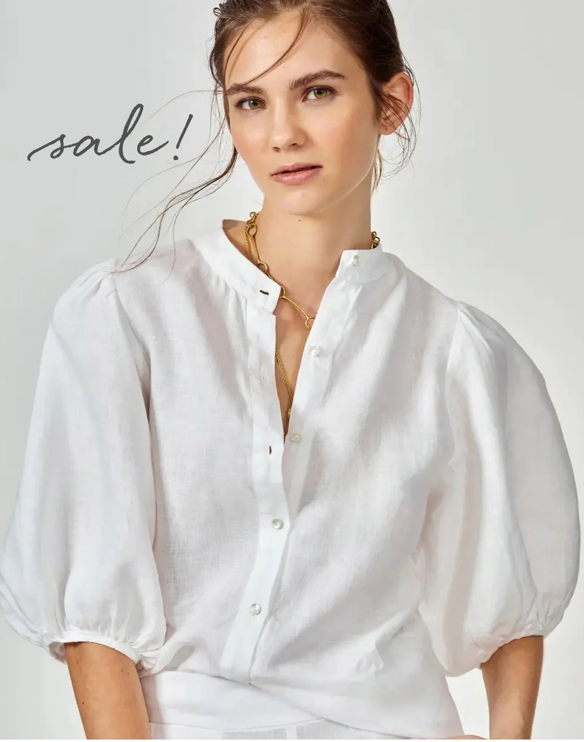 A woman with brunette hair tied back is wearing a white, long-sleeved button-up blouse with puffed sleeves. She has a neutral expression and is standing against a plain background. The word "sale!" is handwritten in script on the top left of the image. Fearrington Village