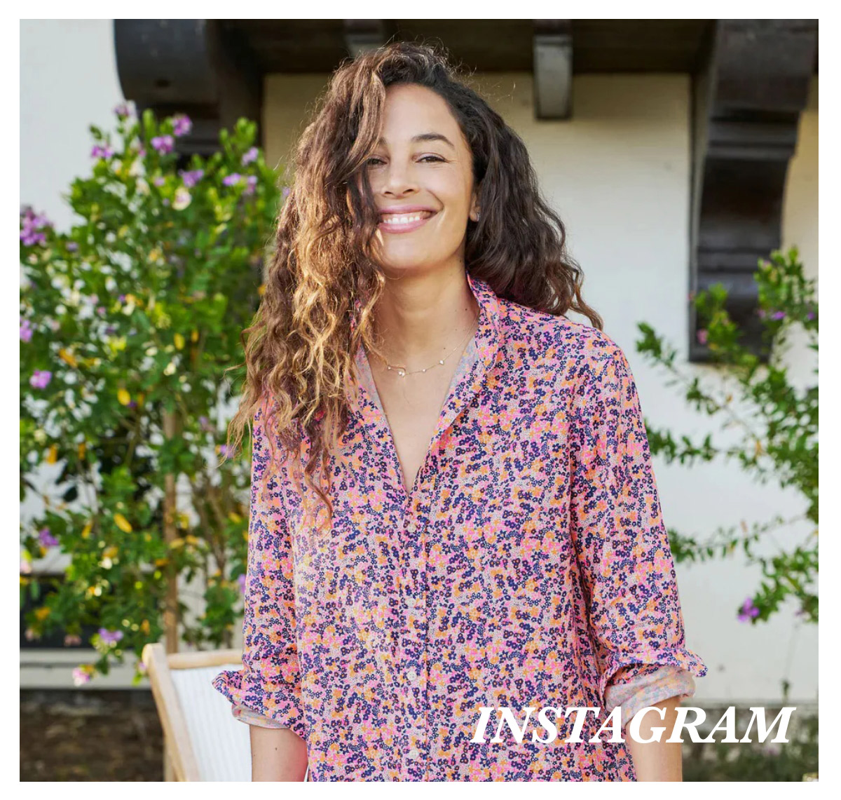 A woman with long curly hair stands outside in front of a building with flowers in the background, smiling and wearing a pink and purple floral blouse. The text "INSTAGRAM" is written in white in the bottom right corner. Fearrington Village