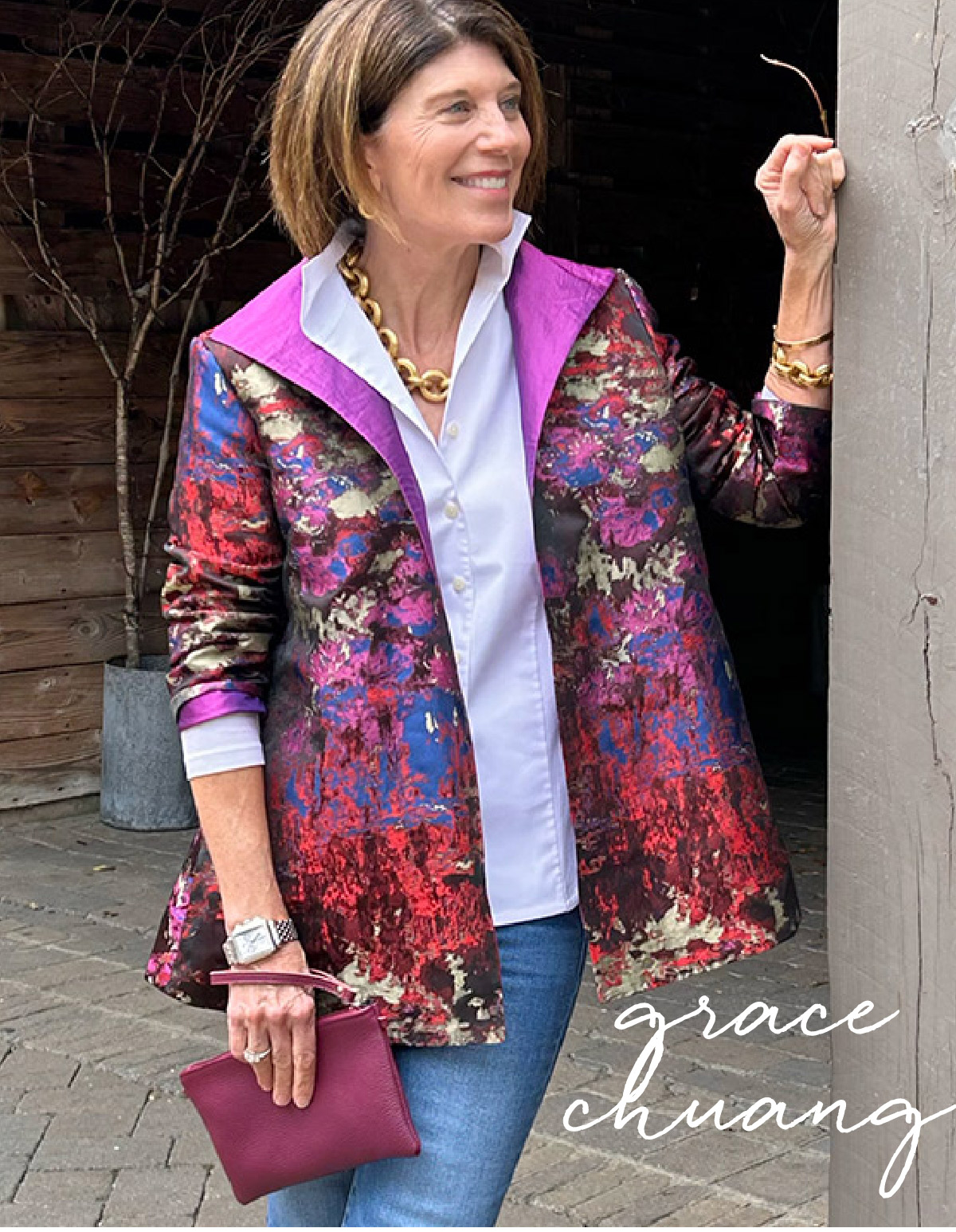 A woman stands outdoors, smiling, wearing a vibrant, colorful jacket over a light blouse, accessorized with a chunky gold necklace and holding a maroon clutch. Her name, Grace Chuang, is written in elegant script in the bottom right corner. Fearrington Village