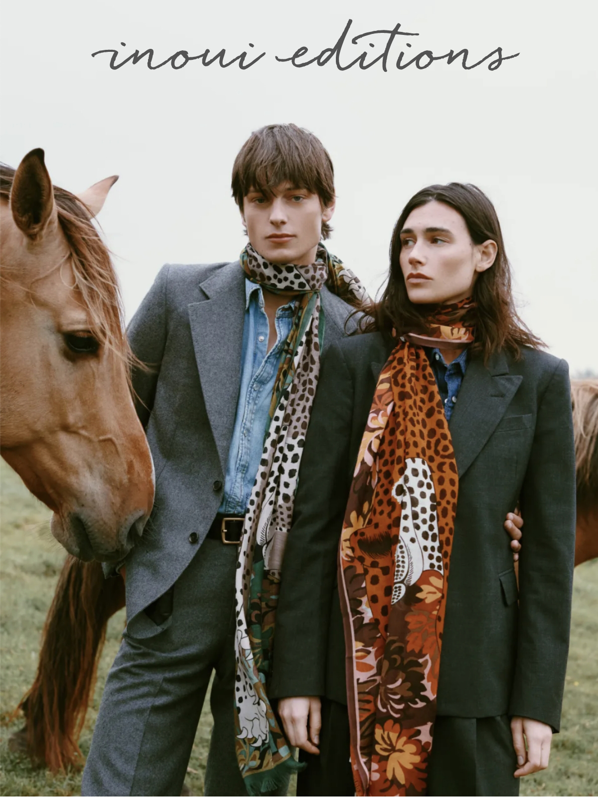 Two people in suits stand outdoors, each wearing patterned scarves. They are next to a brown horse. The logo "inoui editions" is at the top. The background is a grassy field. Fearrington Village