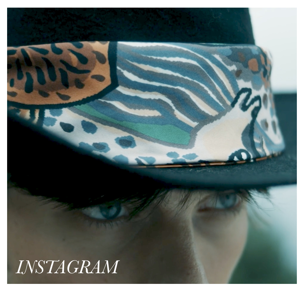 Close-up of a person's eyes partially obscured by the brim of a black hat adorned with a colorful, patterned band. The bottom left corner has the word "INSTAGRAM" in white text. Fearrington Village