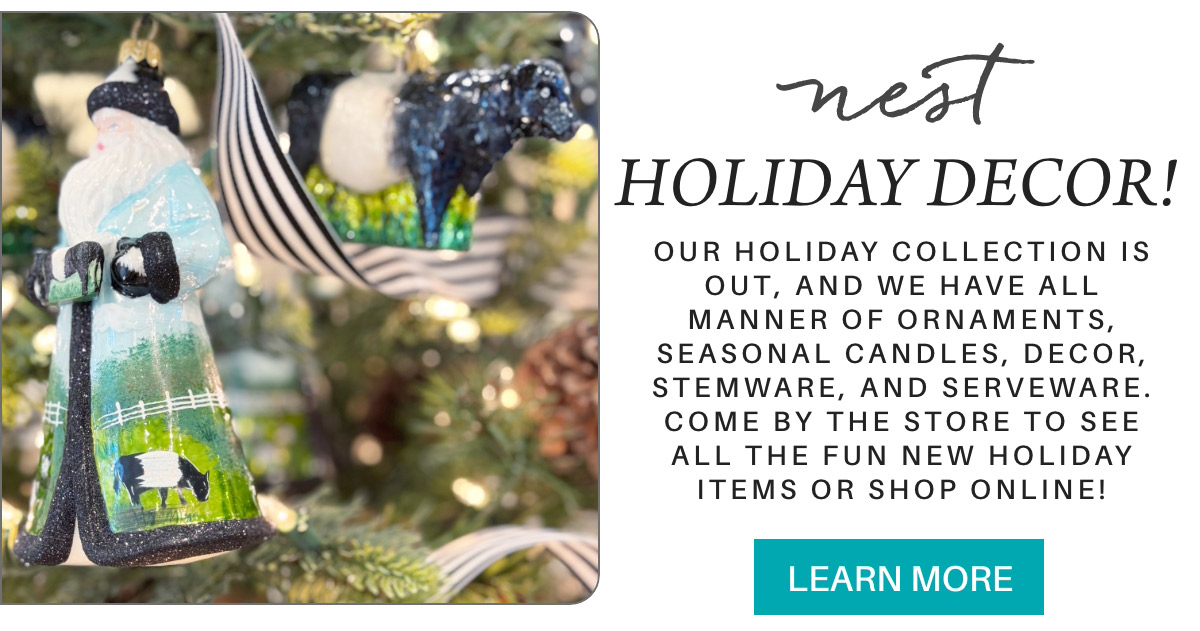 A holiday advertisement showing a close-up of tree ornaments, including a Santa figure and a cow. The text promotes holiday decor, including candles and serveware, inviting people to visit the store or shop online. Fearrington Village