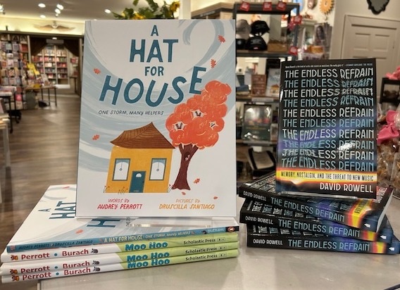 Books displayed on a table in a store, including "A Hat for House" with an illustrated house and tree on the cover, and "The Endless Refrain" with a patterned design. Shelves and more books are visible in the background. Fearrington Village