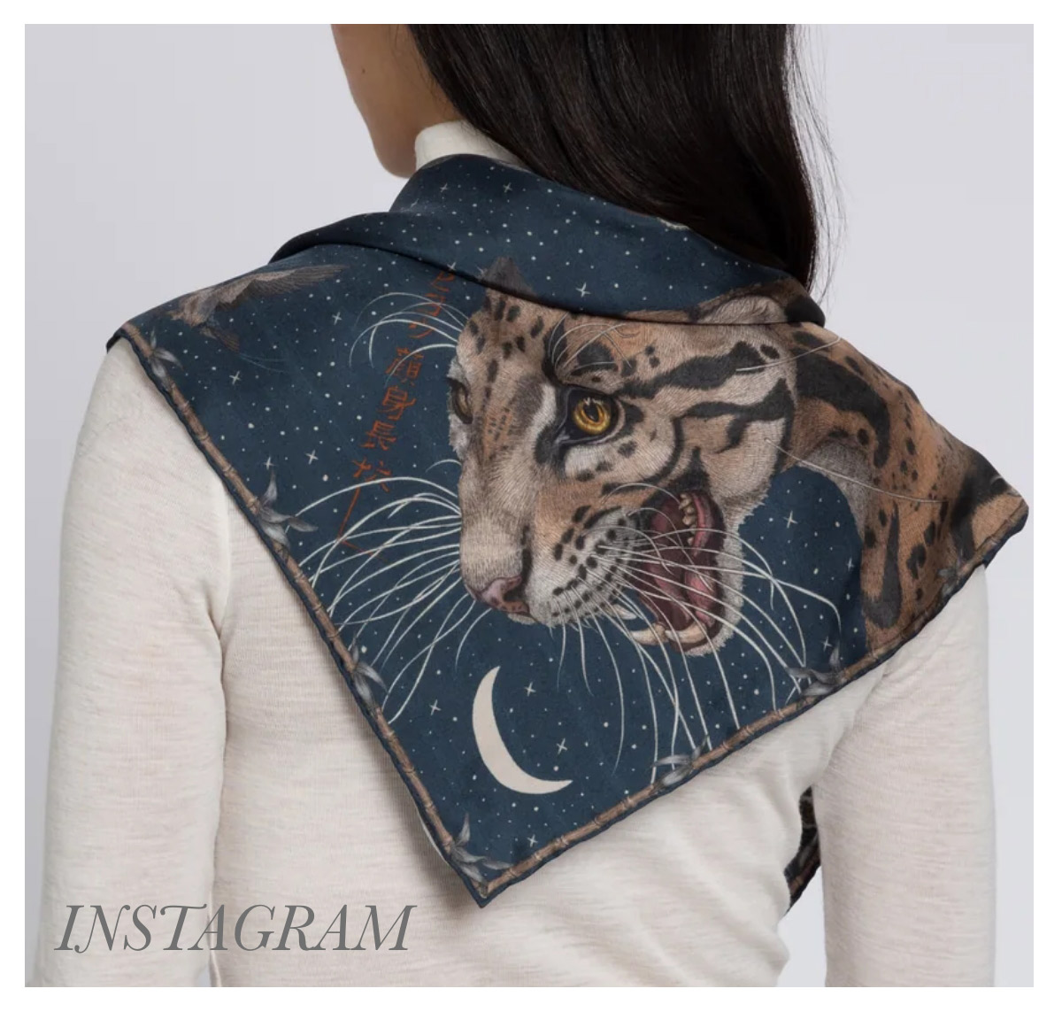 A person wearing a scarf with a tiger design featuring a detailed tiger head against a starry night sky background with a crescent moon. The scarf is draped over the person's shoulders. Fearrington Village