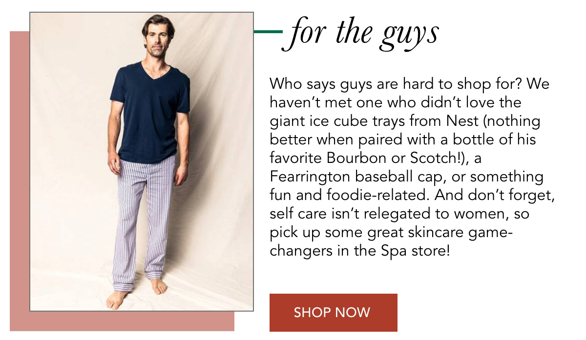 A man wearing a navy T-shirt and gray pajama pants stands on a light background. Text promotes gifts for men, suggesting items like ice cube trays, spirits, sports items, and skincare. A "Shop Now" button is at the bottom. Fearrington Village