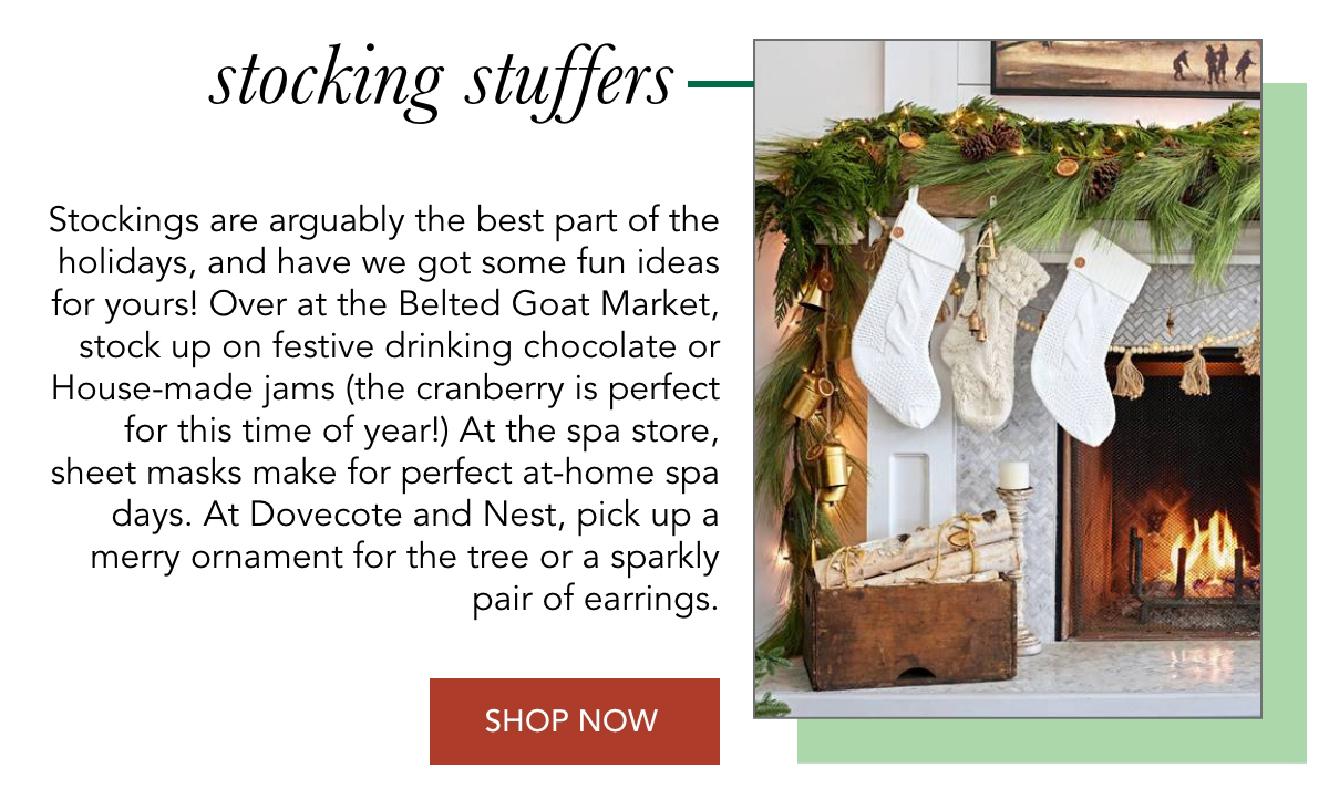 A cozy living room scene with stockings hung over a fireplace decorated with greenery. A text overlay promotes holiday stocking stuffer ideas from various stores, featuring products like drinking chocolate, jams, sheet masks, and ornaments. Fearrington Village