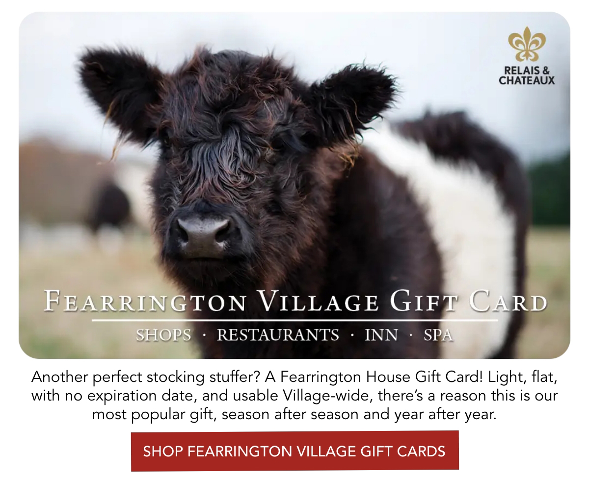 A fluffy black and white cow stands in focus, with text advertising Fearrington Village Gift Cards. The background is blurred, emphasizing the cow. The card is for use at shops, restaurants, an inn, and spa. Fearrington Village