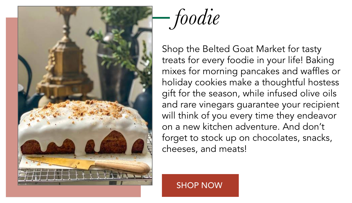 A frosted loaf cake on a cooling rack with a decorative background. Text highlights Belted Goat Market's offerings, including baking mixes, olive oils, and vinegars. A red "Shop Now" button is displayed. Fearrington Village