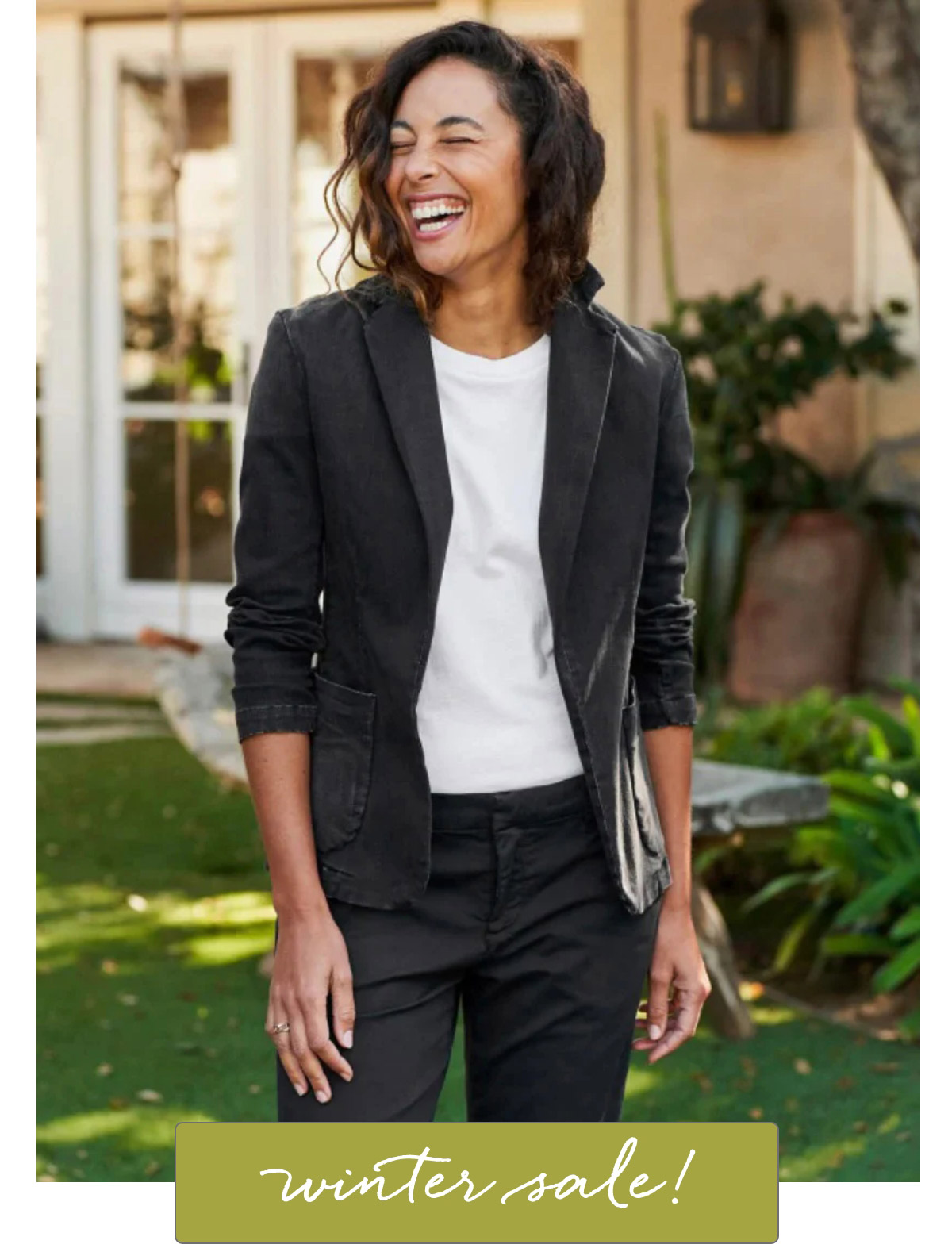 A woman wearing a white shirt and black blazer smiles while standing outside in a garden. There's a text overlay at the bottom that reads, "winter sale!. Fearrington Village