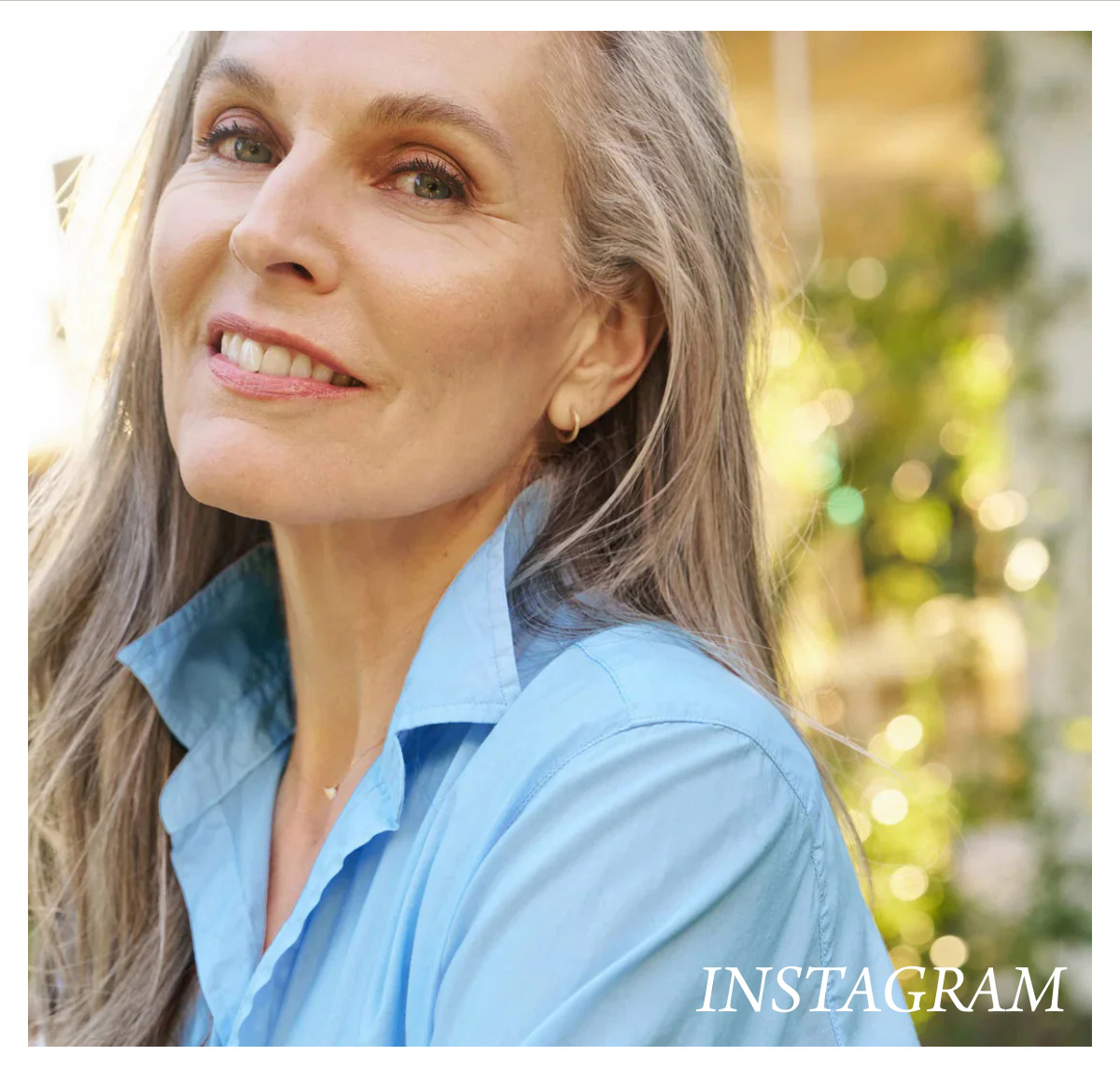 A woman with long gray hair smiles softly at the camera. She is wearing a light blue shirt. The background is softly blurred with green foliage and light. The word "INSTAGRAM" is visible in the bottom right corner. Fearrington Village