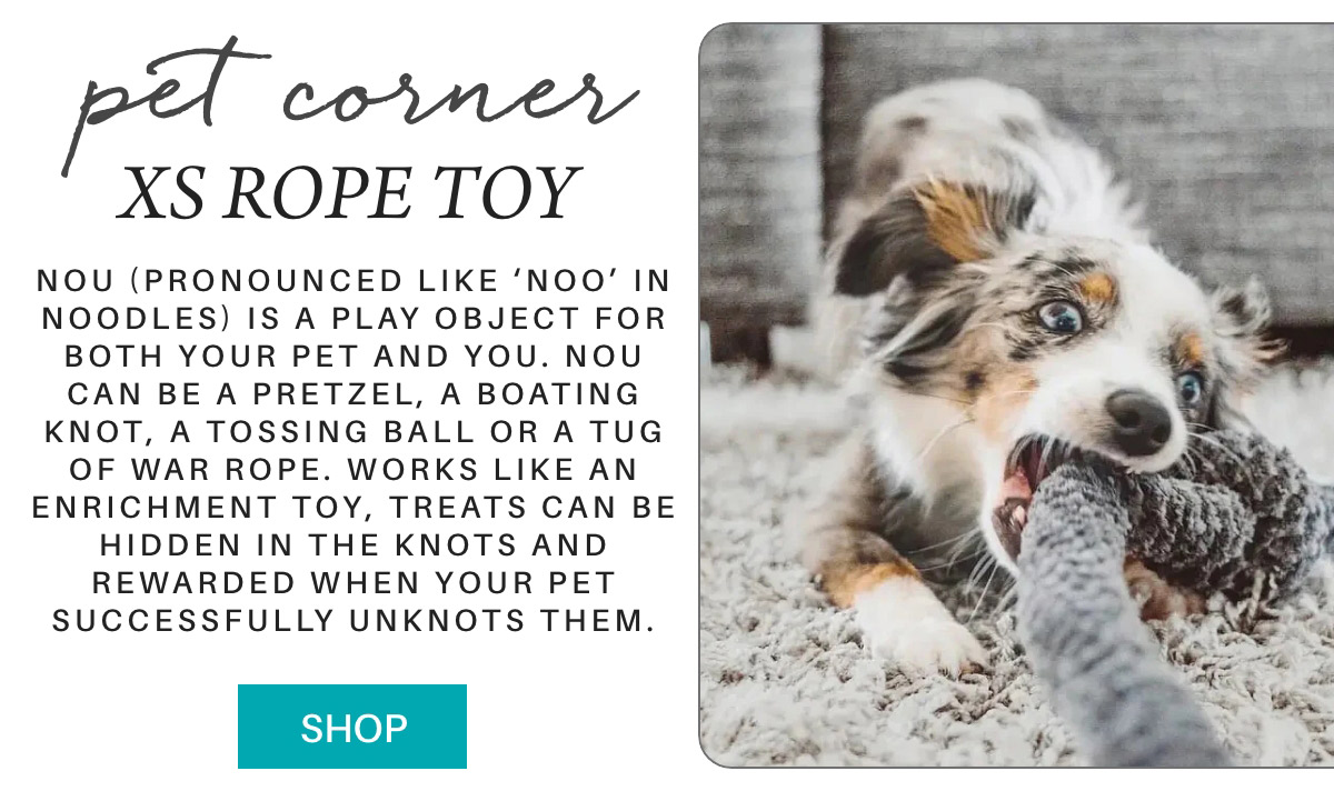 A playful dog chews on a rope toy on a carpet. The text describes the toy as an enrichment item for pets, encouraging them to unravel knots for treats. A "Shop" button is visible at the bottom. Fearrington Village