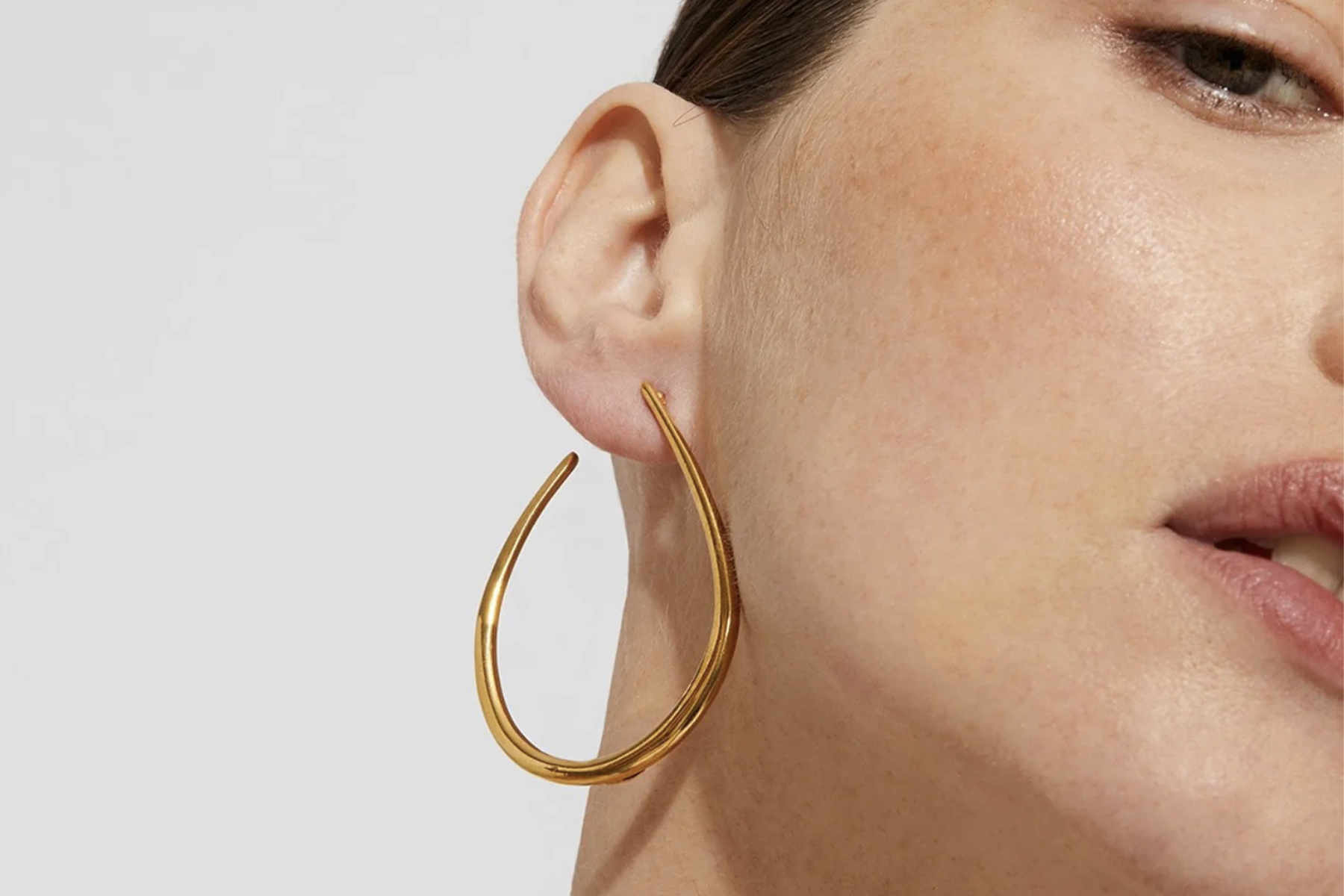 Close-up of a person wearing a large, gold, hoop earring on their left ear. The background is plain, highlighting the earring and the person's skin. Fearrington Village