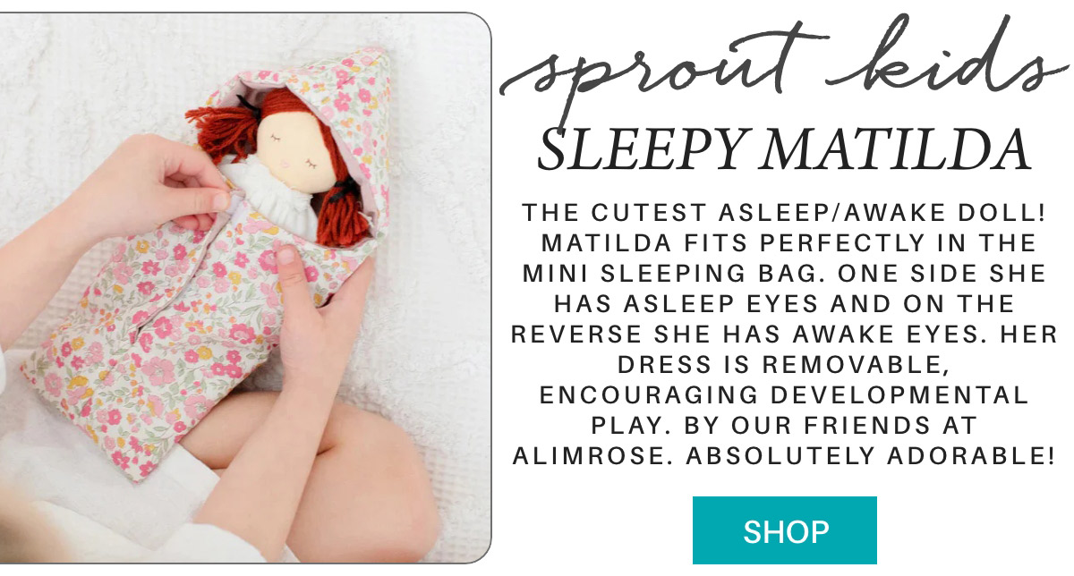 A person places a fabric doll with red yarn hair into a floral mini sleeping bag. The doll has asleep eyes on one side, awake eyes on the other. Text describes the product as a developmental toy. A "Shop" button is visible. Fearrington Village