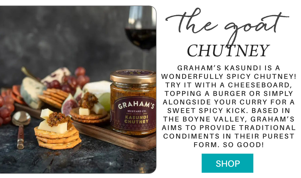 A jar of Graham's Kasundi Chutney sits on a slate board beside cheese, crackers, grapes, and a glass of wine. Text describes it as a spicy chutney perfect for cheeseboards or curries. A button at the bottom reads "Shop. Fearrington Village