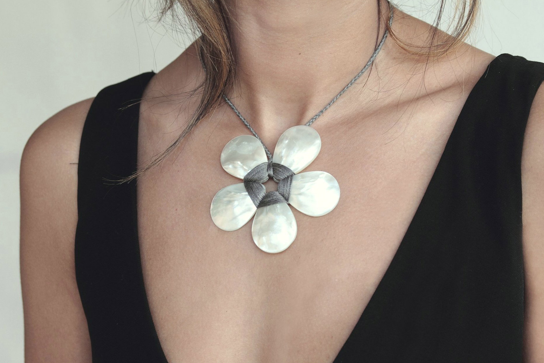 A woman wearing a black V-neck top showcases a necklace with a large, flower-shaped pendant made of silver petals. The necklace is centered on her chest. Fearrington Village