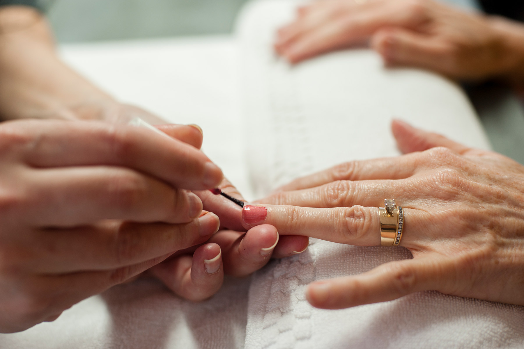 The Spa Edit - Time To Pamper Mom 1 A person is applying pink nail polish to someone else's nails. The hands rest on a white towel, and the person receiving the manicure is wearing a gold ring with a stone. Fearrington Village