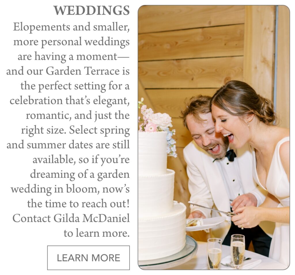 A joyful bride and groom in formal attire laugh as they cut a white, tiered wedding cake together in a rustic, wood-paneled venue decorated with flowers. "Elopements and smaller, more personal weddings are having a moment—and our Garden Terrace is the perfect setting for a celebration that’s elegant, romantic, and just the right size. Select spring and summer dates are still available, so if you’re dreaming of a garden wedding in bloom, now’s the time to reach out! Contact Gilda McDaniel to learn more." Fearrington Village