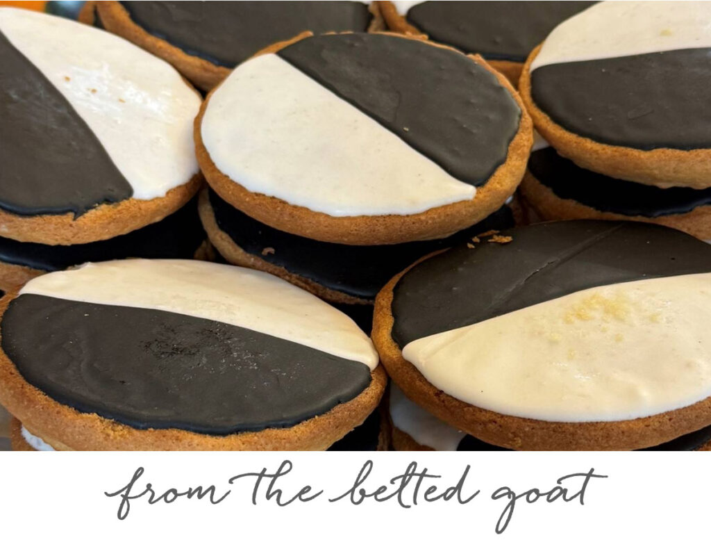 The Fearrington Plate - May 1, 2025 4 A close-up of black and white cookies stacked together. Each cookie is half frosted with black icing and half with white icing. Below the cookies, handwritten text reads: "from the betted goat. Fearrington Village