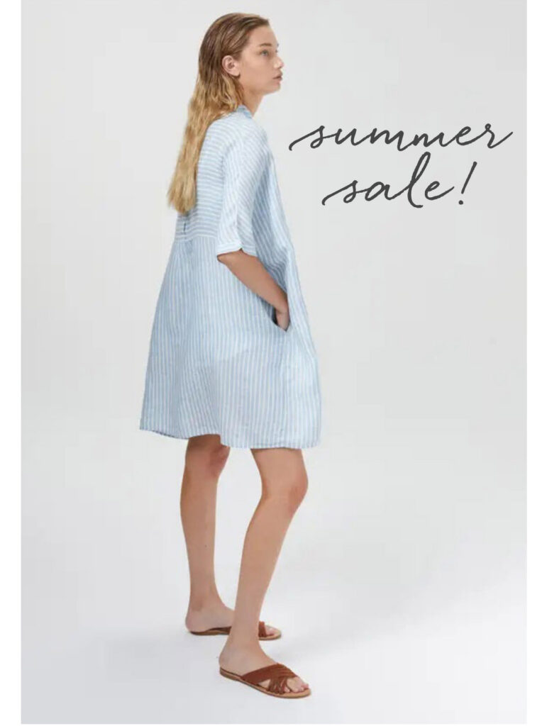 Woman wearing a light blue striped dress and brown sandals, standing sideways with hands in pockets. Text reads "summer sale!" on a plain white background. Fearrington Village