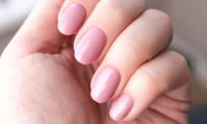 A close-up of a hand with neatly manicured nails painted in a glossy, light pink color. The nails are oval-shaped and the skin appears smooth and well-groomed. Fearrington Village