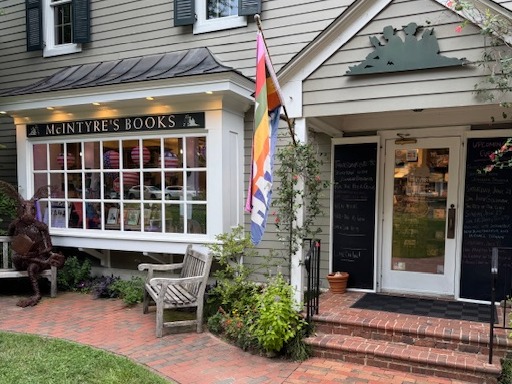Gentle Reader - June 17, 2025 1 A quaint bookstore called McIntyre’s Books with a large front window, a rainbow pride flag, a metal sculpture bench, and chalkboard signs outside, surrounded by greenery and brick pavement. Fearrington Village