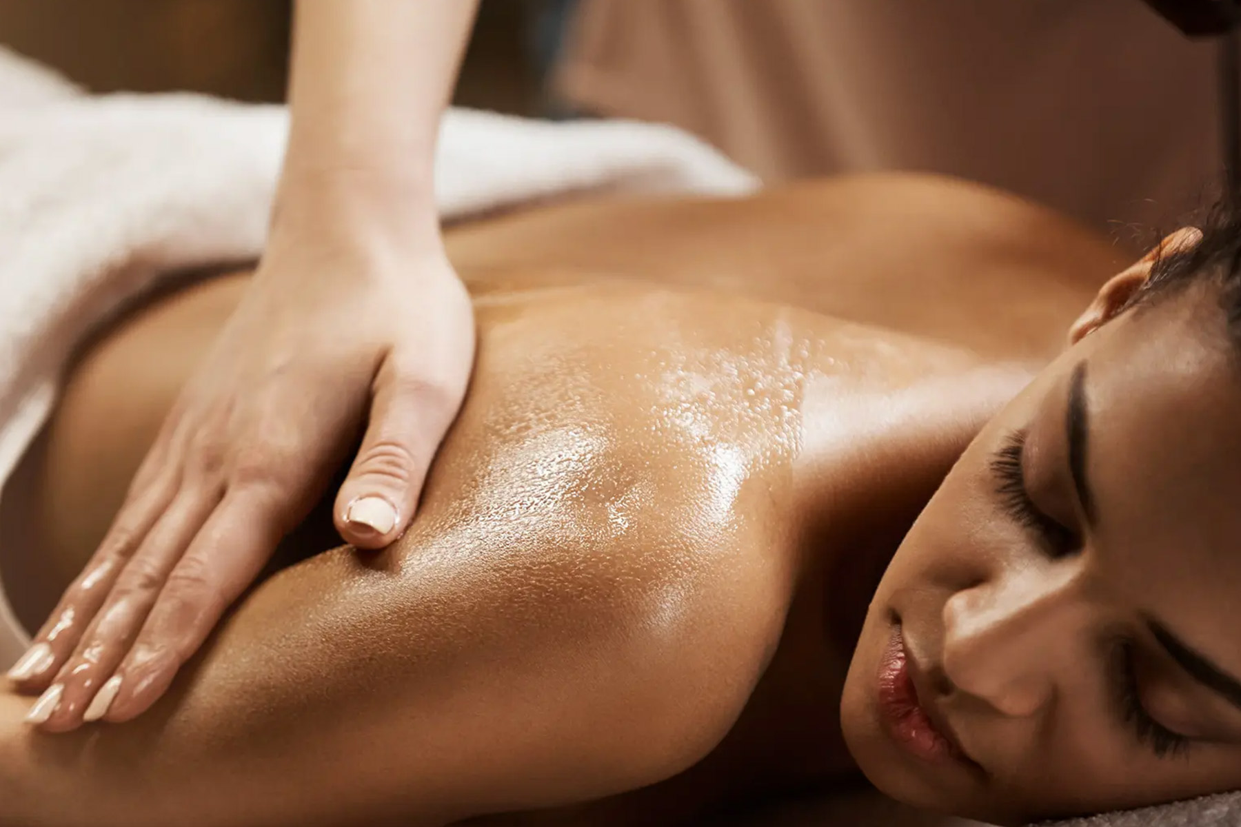 The Spa Edit - Get Beach Ready 1 A person lying face down on a massage table receives a relaxing shoulder massage with oil, their eyes closed in comfort. Fearrington Village