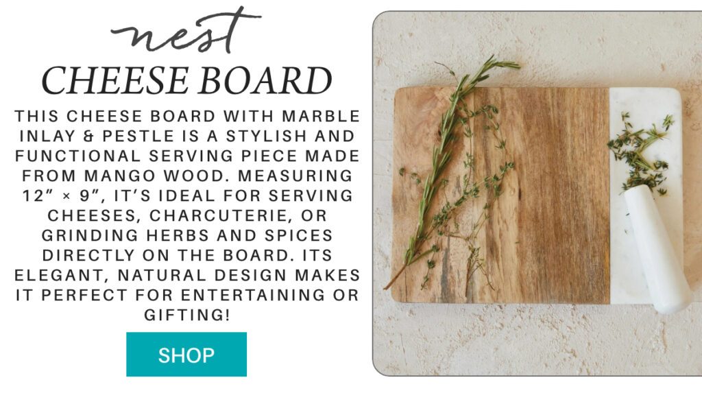 A wooden cheese board with a marble inlay and white marble pestle, topped with sprigs of fresh herbs, is displayed beside a product description and a turquoise "Shop" button. "This Cheese Board with Marble inlay & Pestle is a stylish and functional serving piece made from mango wood. Measuring 12” × 9”, it’s ideal for serving cheeses, charcuterie, or grinding herbs and spices directly on the board. Its elegant, natural design makes it perfect for entertaining or gifting!" Fearrington Village